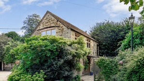 A stone house with a sloped roof, surrounded by dense greenery and a paved driveway. - 2 bedroom accommodation in Uley, near Dursley (Uley, near Dursley)