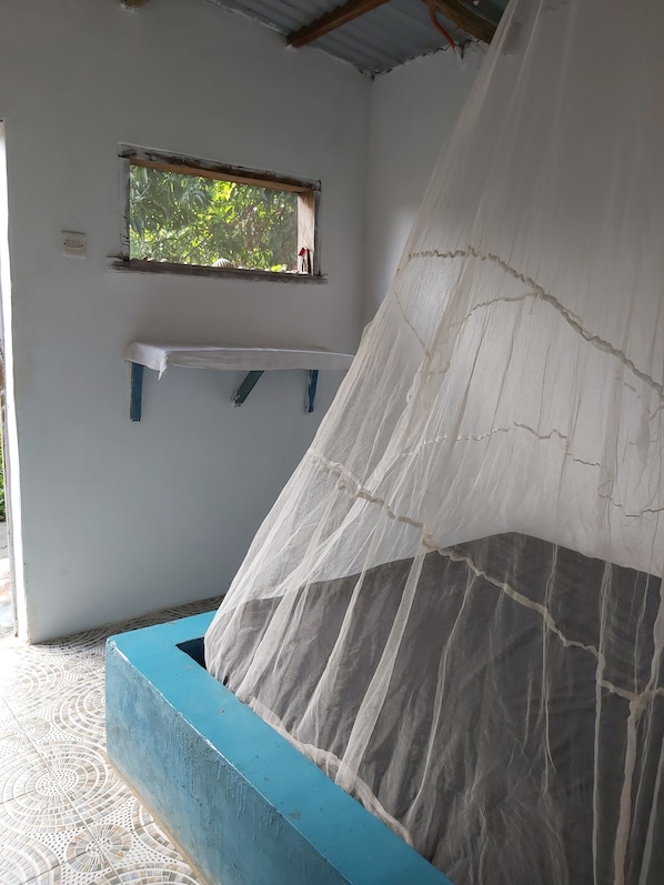 A room with a bed covered by a white mosquito net, a small window, and a blue wall.