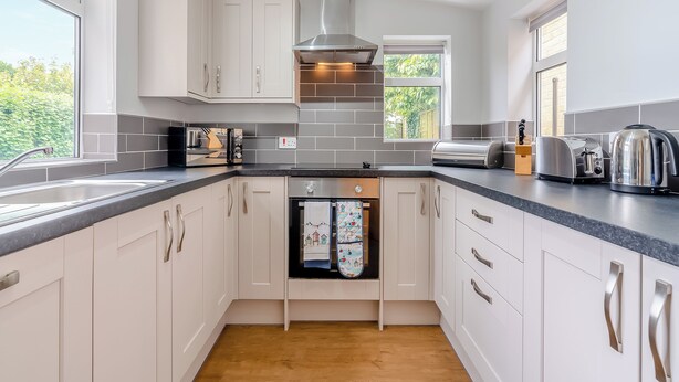 A modern kitchen with white cabinets, stainless steel appliances, and a wooden floor.