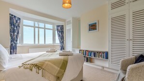 A bedroom with a bed, a window with curtains, a bookshelf, and a chair.
