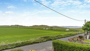 A rural road with a stone wall and hedge on one side, and a green field on the other.