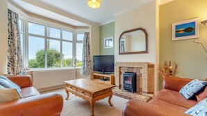 A living room with leather sofas, a wooden coffee table, a television, a fireplace, and large windows with curtains.