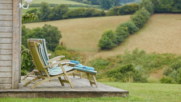 A wooden deck with two striped lounge chairs and a lamp post, overlooking a rural landscape with fields and trees. - 1 bedroom accommodation in Sidbury, near Sidmouth (Sidbury, near Sidmouth)