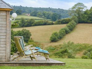 A wooden deck with two striped lounge chairs and a lamp post, overlooking a rural landscape with fields and trees.