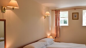 A neatly made bed with white linens, two wall-mounted lamps, a window with curtains, and a framed picture on the wall. - 1 bedroom accommodation in Sidbury, near Sidmouth (Sidbury, near Sidmouth)