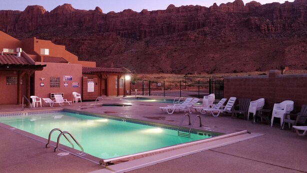 A swimming pool with lounge chairs and a building with a red-tiled roof. - Slickrock Sands - Sleeps 8! Pet/bike friendly. (Moab)