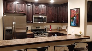 A kitchen with dark wood cabinets, stainless steel appliances, a granite countertop, and a painting of a waterfall on the wall. - Slickrock Sands - Sleeps 8! Pet/bike friendly. (Moab)