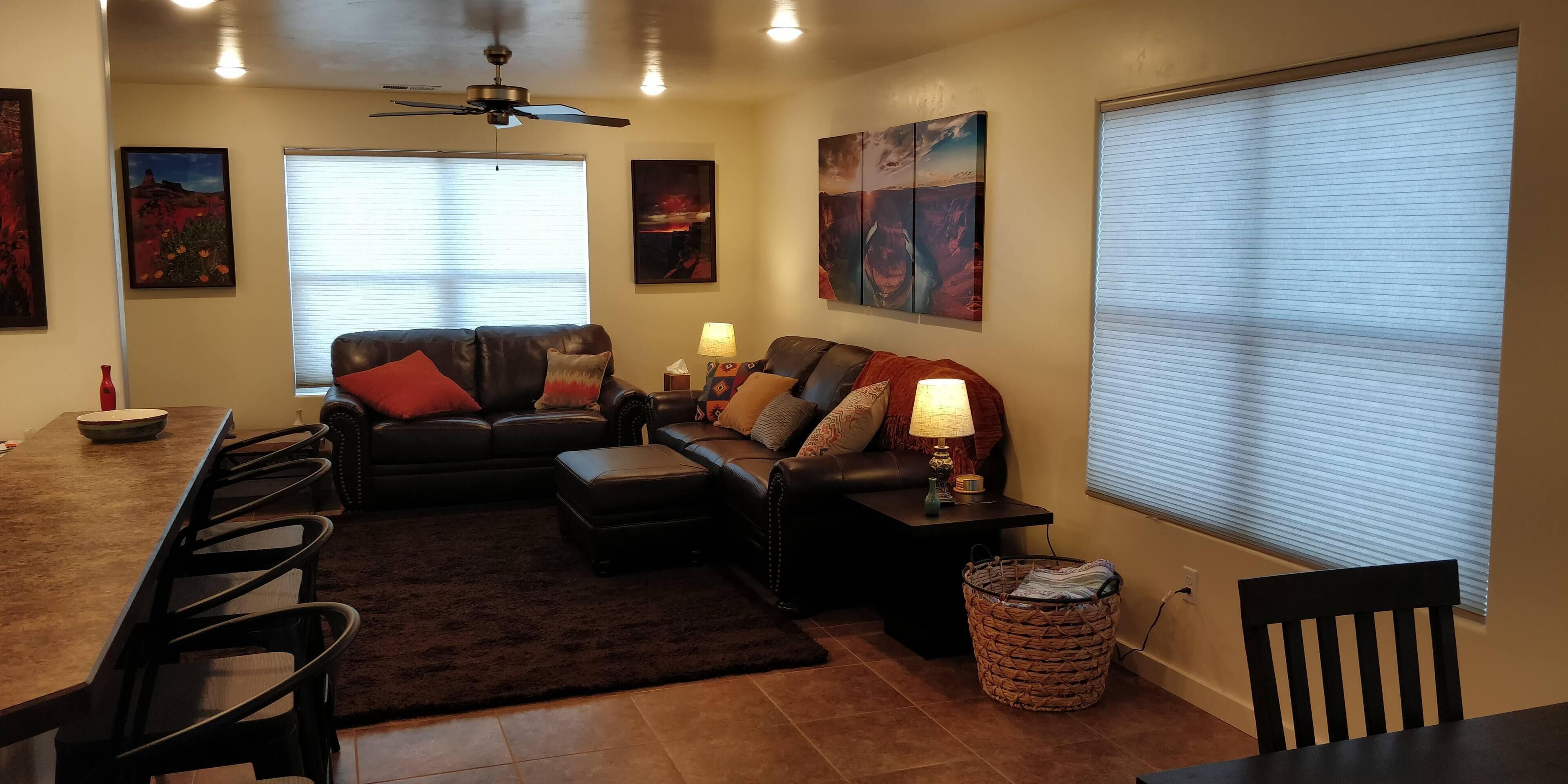 A living room with a sofa, a coffee table, a dining table with chairs, a ceiling fan, and artwork on the walls.