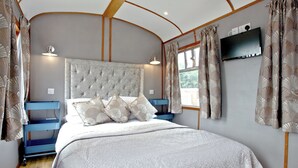 Quarto com cabeceira estofada, cama com roupa de cama branca, mesa de cabeceira azul e janela com cortinas.