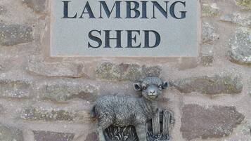 Un muro de piedra con un cartel que dice "LAMBING SHED" y una escultura de oveja.