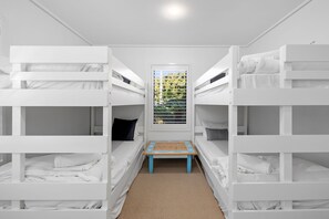 Une chambre avec un lit superposé, une petite table et une fenêtre avec des stores.