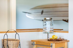 A room with a wooden table, a wicker basket, a glass jar, and a surfboard on the wall.