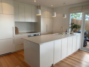 Une cuisine moderne avec des meubles blancs, un îlot central, des luminaires suspendus et une vue sur l’extérieur.