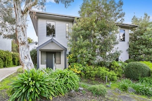 A two-story residential building with a front entrance, a small porch, and a well-maintained garden with various plants and shrubs. - Fern - Ocean Views, Middle Of Town Pet Friendly (Lorne)