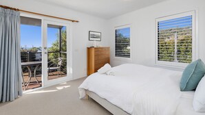 Une chambre à coucher avec un lit, une commode, une chaise et une vue par la fenêtre.