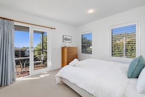 A bedroom with a bed, a dresser, a chair, and a view through a window. - Fern - Ocean Views, Middle Of Town Pet Friendly (Lorne)