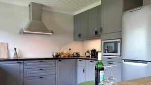 Una cocina moderna con armarios grises, microondas integrado y una mesa de madera con una botella y un bol de pasteles.