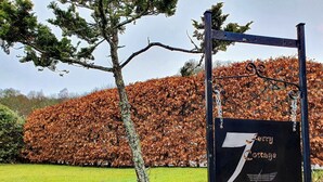 Un cartel que indica '7 Lorry Cottage' con un gran árbol de fondo cubierto de hojas otoñales.