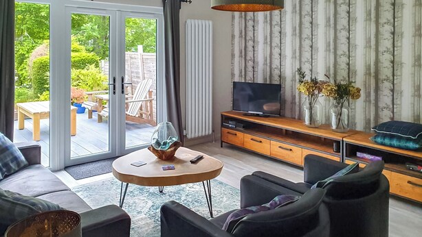 Una sala de estar moderna con un sofá, sillones, una mesa de centro y un televisor sobre un mueble de madera.