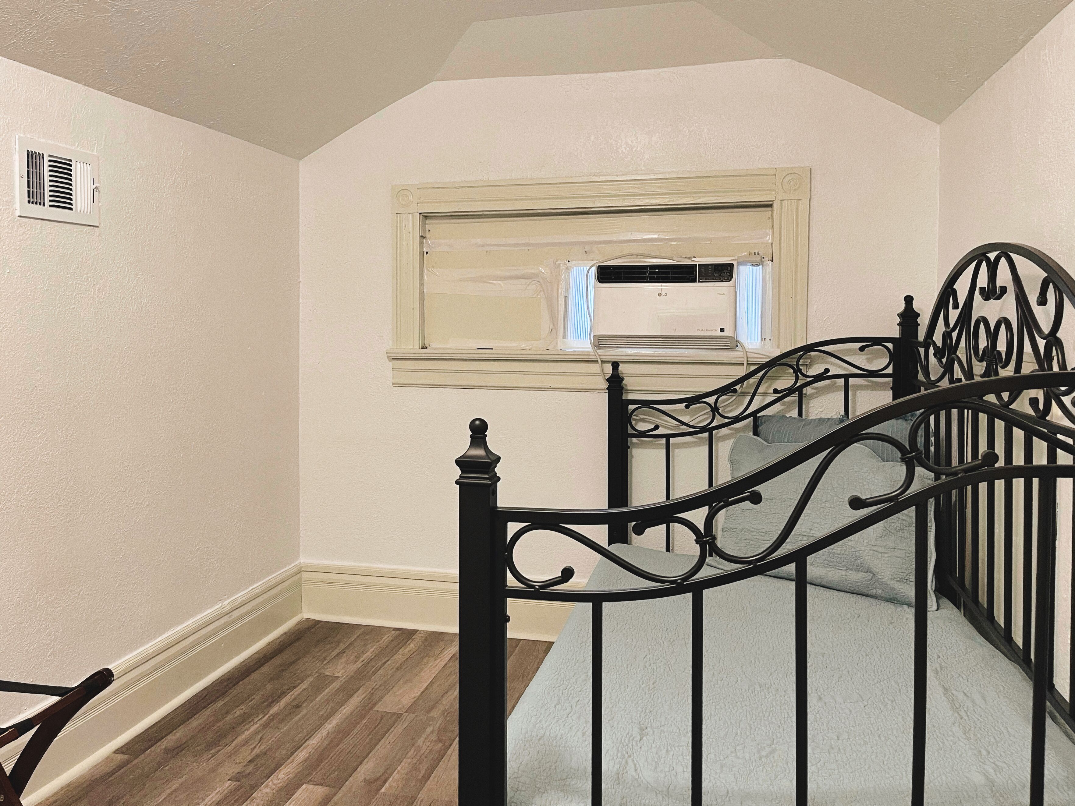 A staircase with a black metal railing, a window with an air conditioner, and a wooden floor.