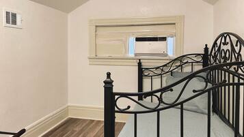 A staircase with a black metal railing, a window with an air conditioner, and a wooden floor.