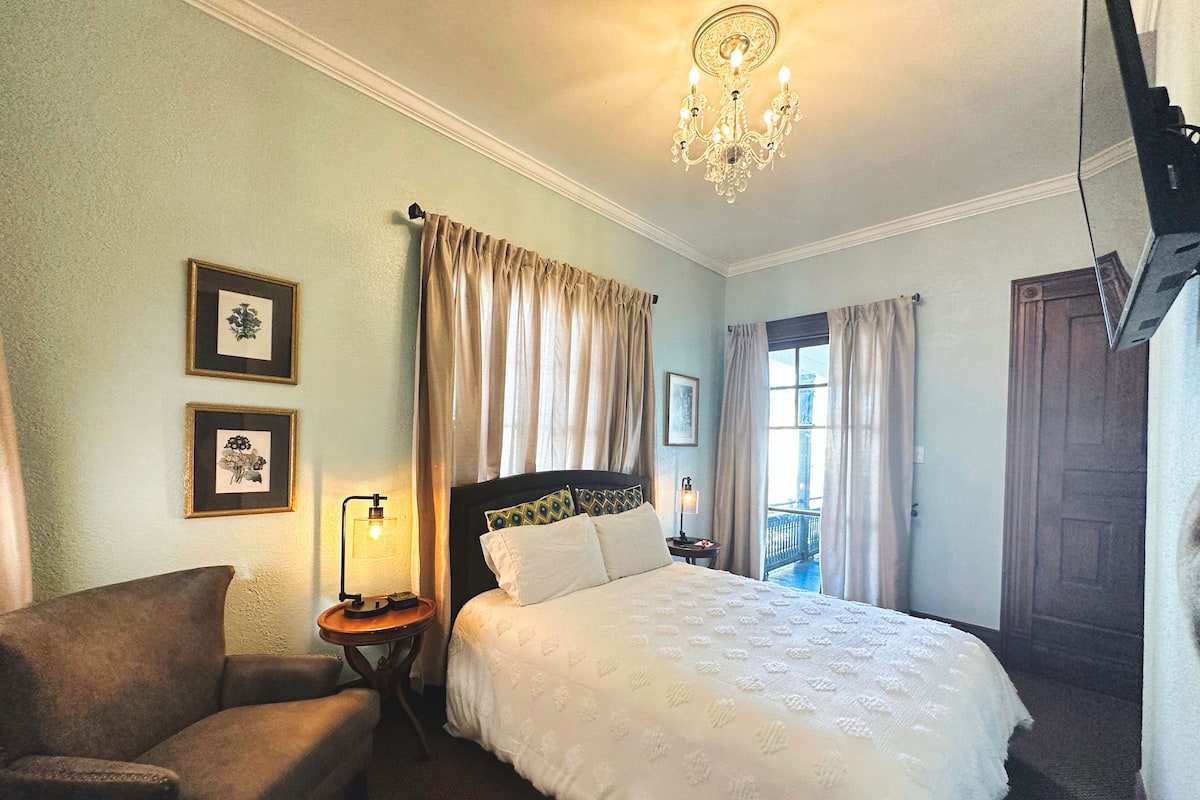 Une chambre d’hôtel avec un lit, une chaise, une table de chevet avec une lampe et un lustre.