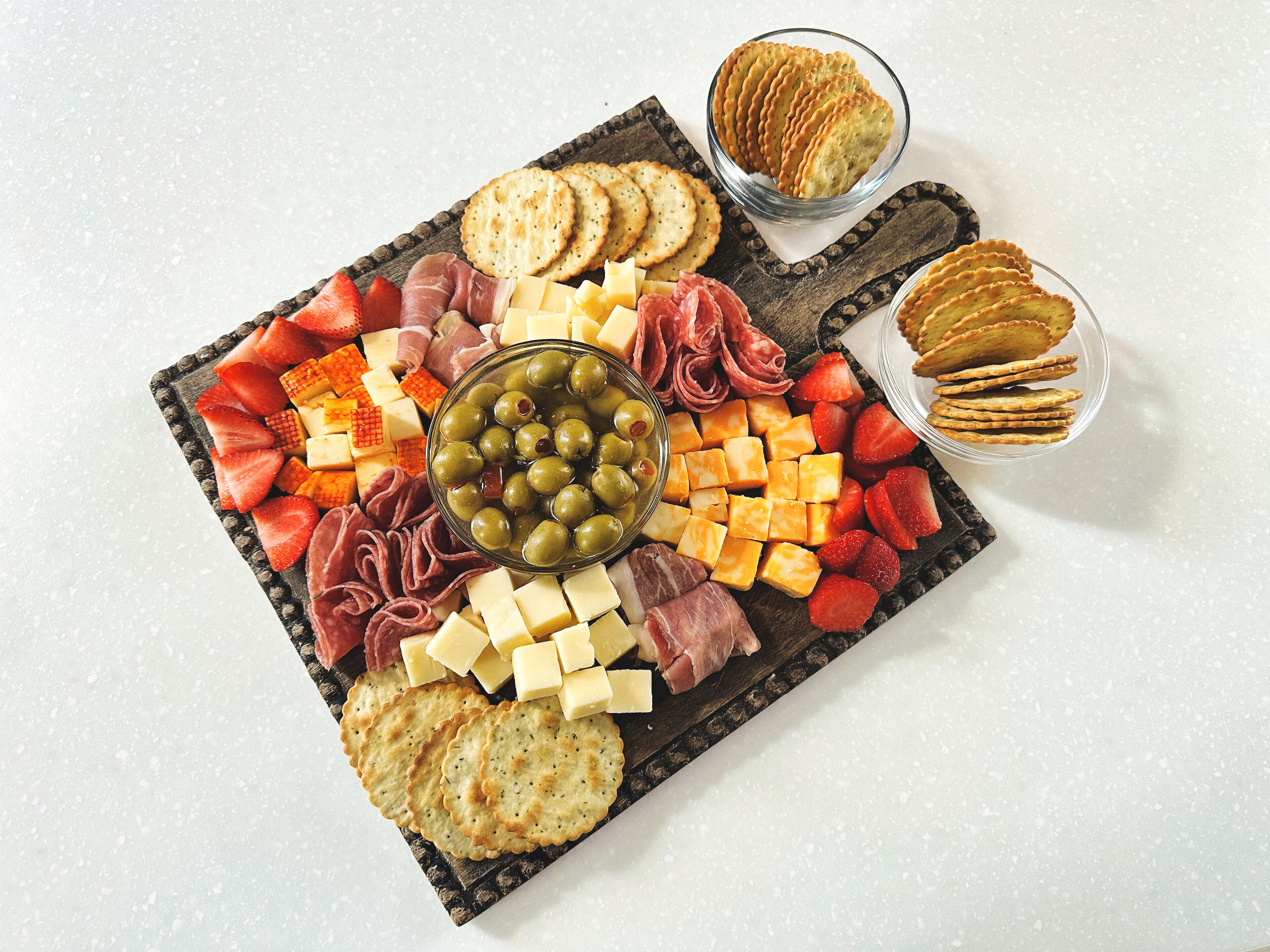 Una tabla de embutidos con varios quesos, carnes y galletas.