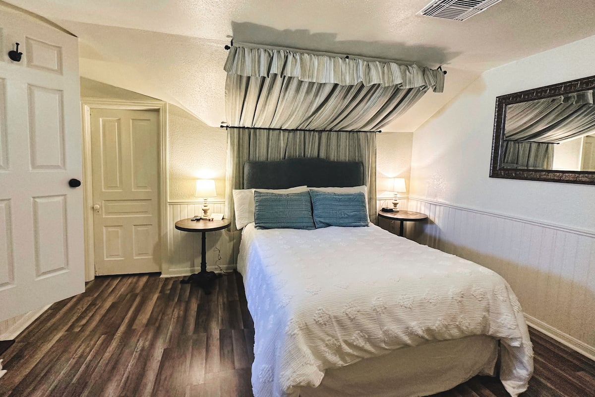 Une chambre à coucher avec un grand lit, deux tables de chevet avec des lampes, une tête de lit, une porte et un miroir au mur.