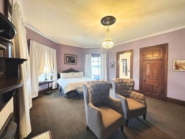 A hotel room with a large bed, two armchairs, a chandelier, and a wooden door.
