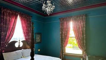 A bedroom with a four-poster bed, a chandelier, and a view of the outdoors through a window with curtains.