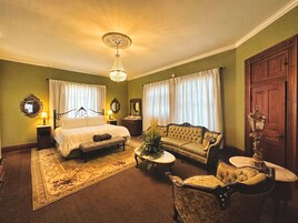 A traditional room with a bed, sofa, armchair, and a chandelier.