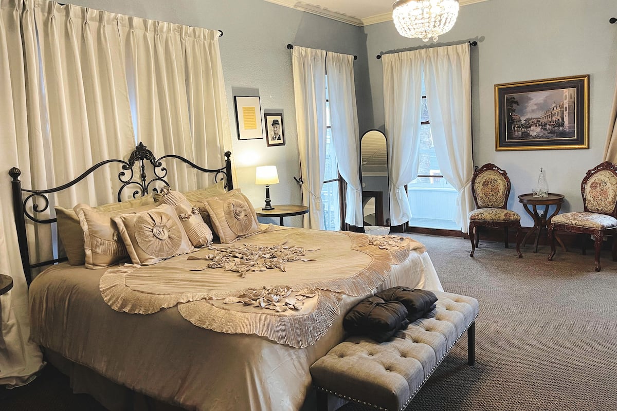 Une chambre à coucher classique, avec un lit à baldaquin, un lustre et une vue sur l’extérieur.