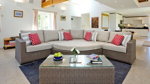 A modern living room with a sectional sofa, a glass coffee table, and a kitchen in the background.