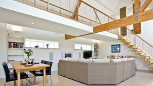 A spacious living area with a dining table, chairs, a sofa, a staircase, and bookshelves.