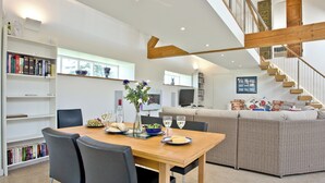 A modern living room with a dining table, chairs, a sofa, a staircase, and bookshelves.