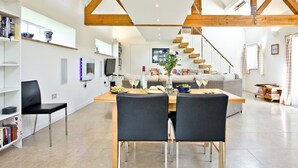 A spacious living area with a dining table, chairs, a sofa, a staircase, and a bookshelf.