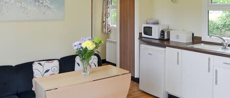 A compact kitchen with a microwave, toaster, and sink. There's a dining area with a table and chairs, and a sofa. A vase with flowers is on the table.