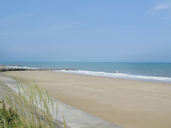 A beach with a concrete walkway and a wooden pier extending into the water. - White Moth - UK12697 (Stalham)