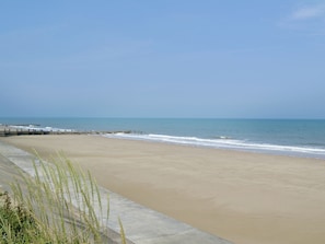 A beach with a concrete walkway and a wooden pier extending into the water. - White Moth - UK12697 (Stalham)