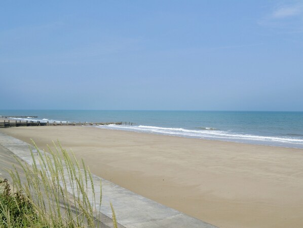 A beach with a concrete walkway and a wooden pier extending into the water. - White Moth - UK12697 (Stalham)