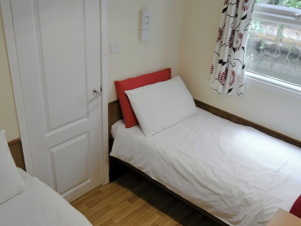 A small, single-bed room with a wooden floor, a white door, and a window with floral curtains. - White Moth - UK12697 (Stalham)