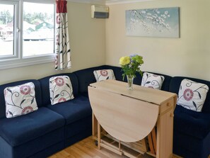 A living room with a dark blue sofa, floral cushions, a small wooden table, and a vase with flowers. - White Moth - UK12697 (Stalham)