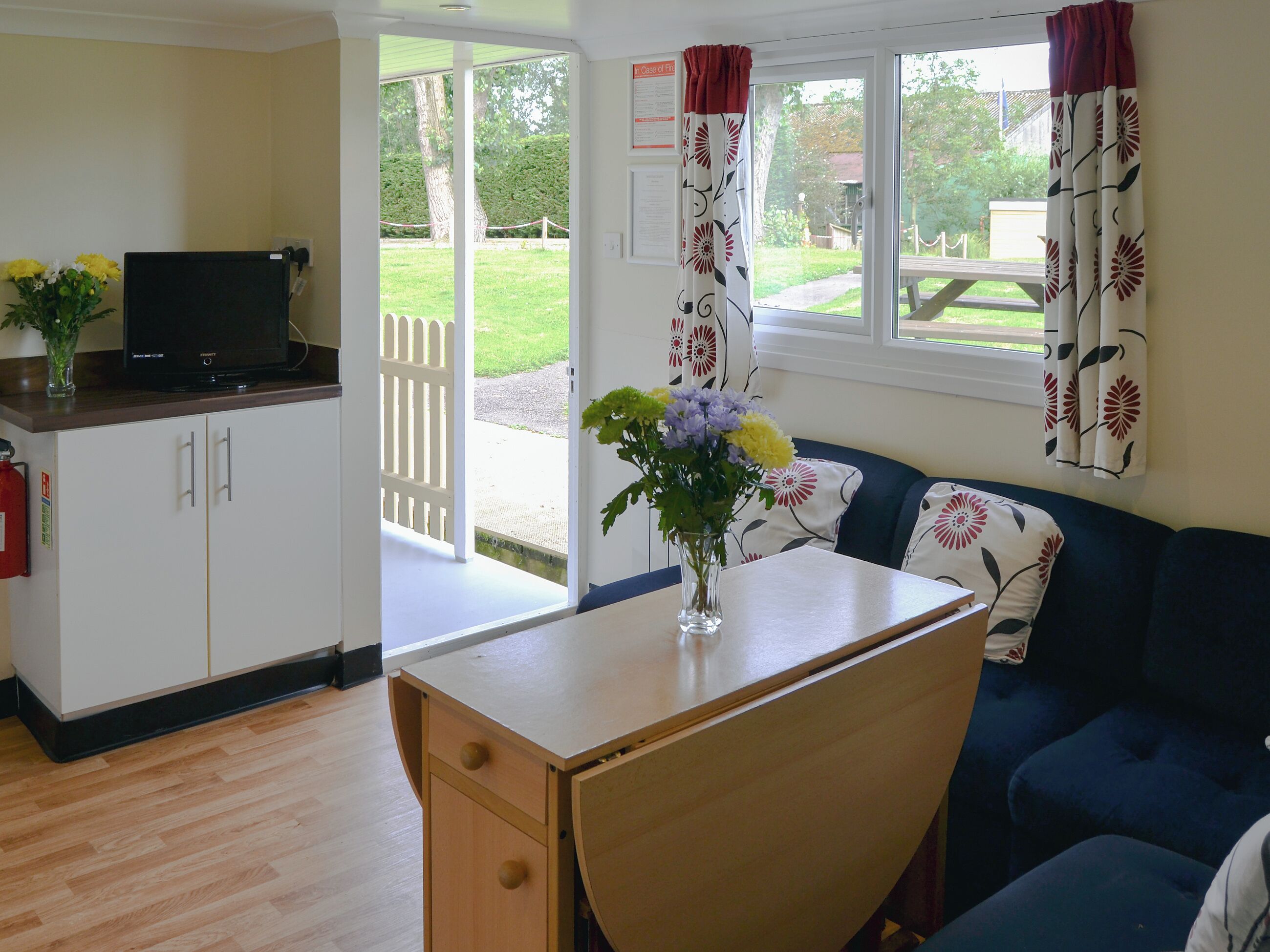 A room with a wooden desk, a blue sofa, a television on a cabinet, and a window with curtains.