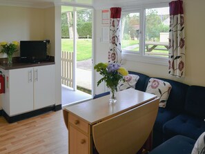 A room with a wooden desk, a blue sofa, a television on a cabinet, and a window with curtains. - White Moth - UK12697 (Stalham)