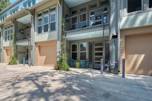 Um edifício de dois andares com uma garagem à direita, uma varanda no segundo andar e uma pequena área externa com cadeiras.
