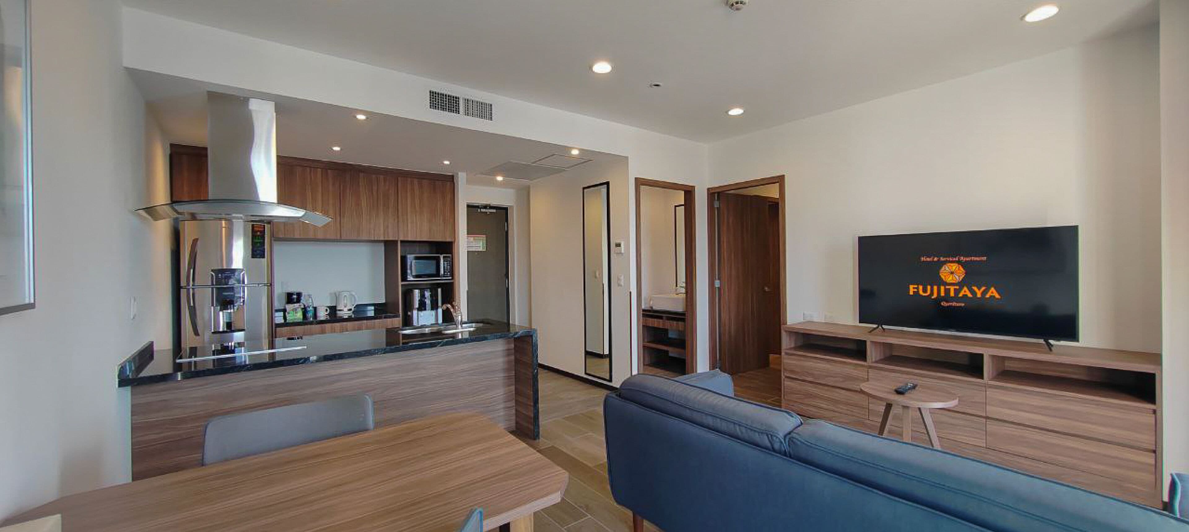Una habitación de hotel moderna con kitchenette, un sofá, un televisor y una mesa de comedor de madera.
