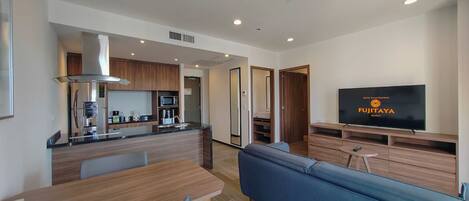 Una habitación de hotel moderna con kitchenette, un sofá, un televisor y una mesa de comedor de madera.