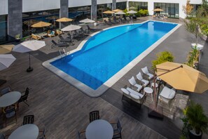 Un espace piscine aménagé sur le toit, avec des chaises longues, des parasols et un bâtiment moderne en arrière-plan.