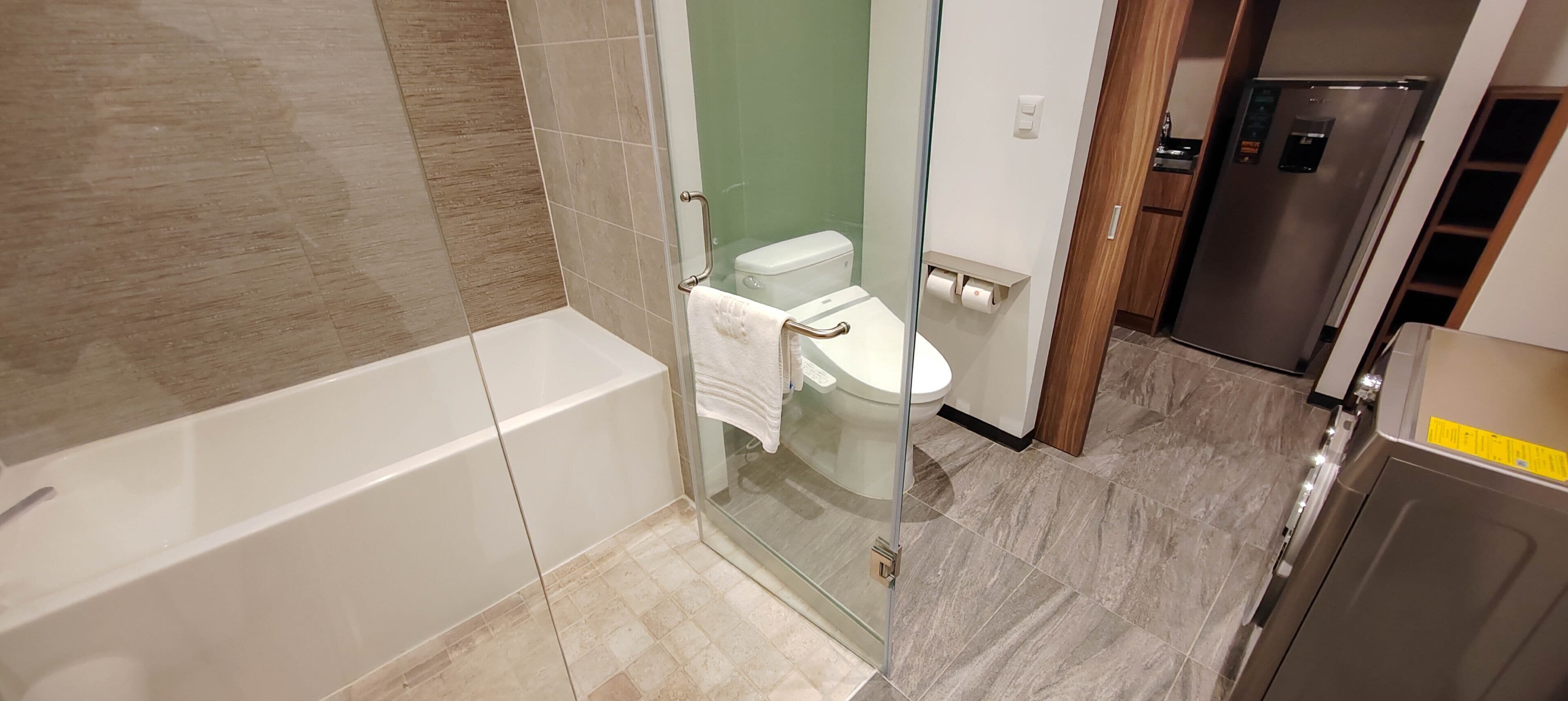 A modern bathroom with a glass-enclosed shower, a white toilet, and a stainless steel refrigerator.