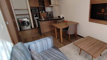 Una habitación de hotel compacta con kitchenette, un sofá, una mesita y un televisor montado en la pared.